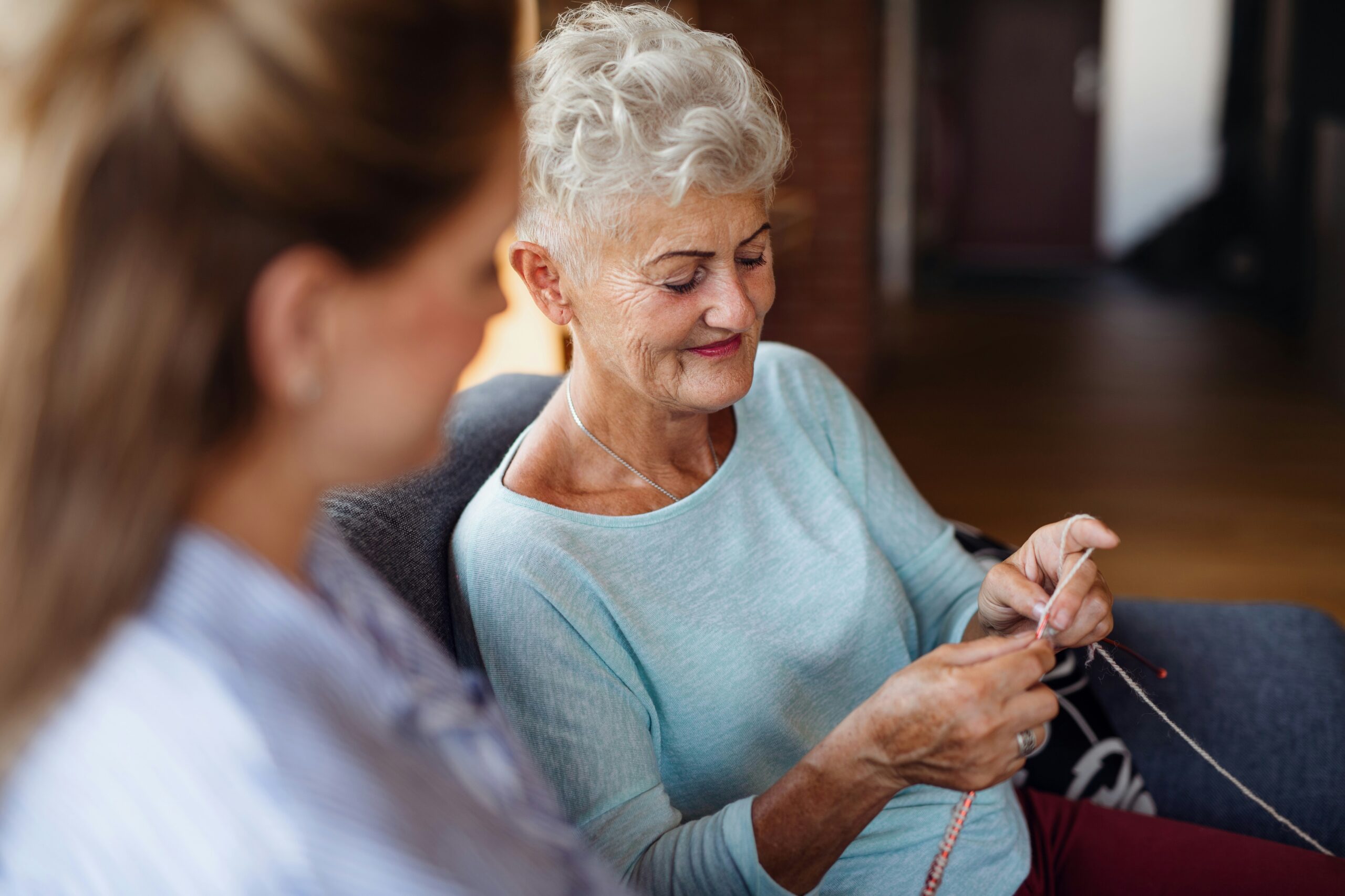Senior woman knits beside her carer, sharing a warm moment.