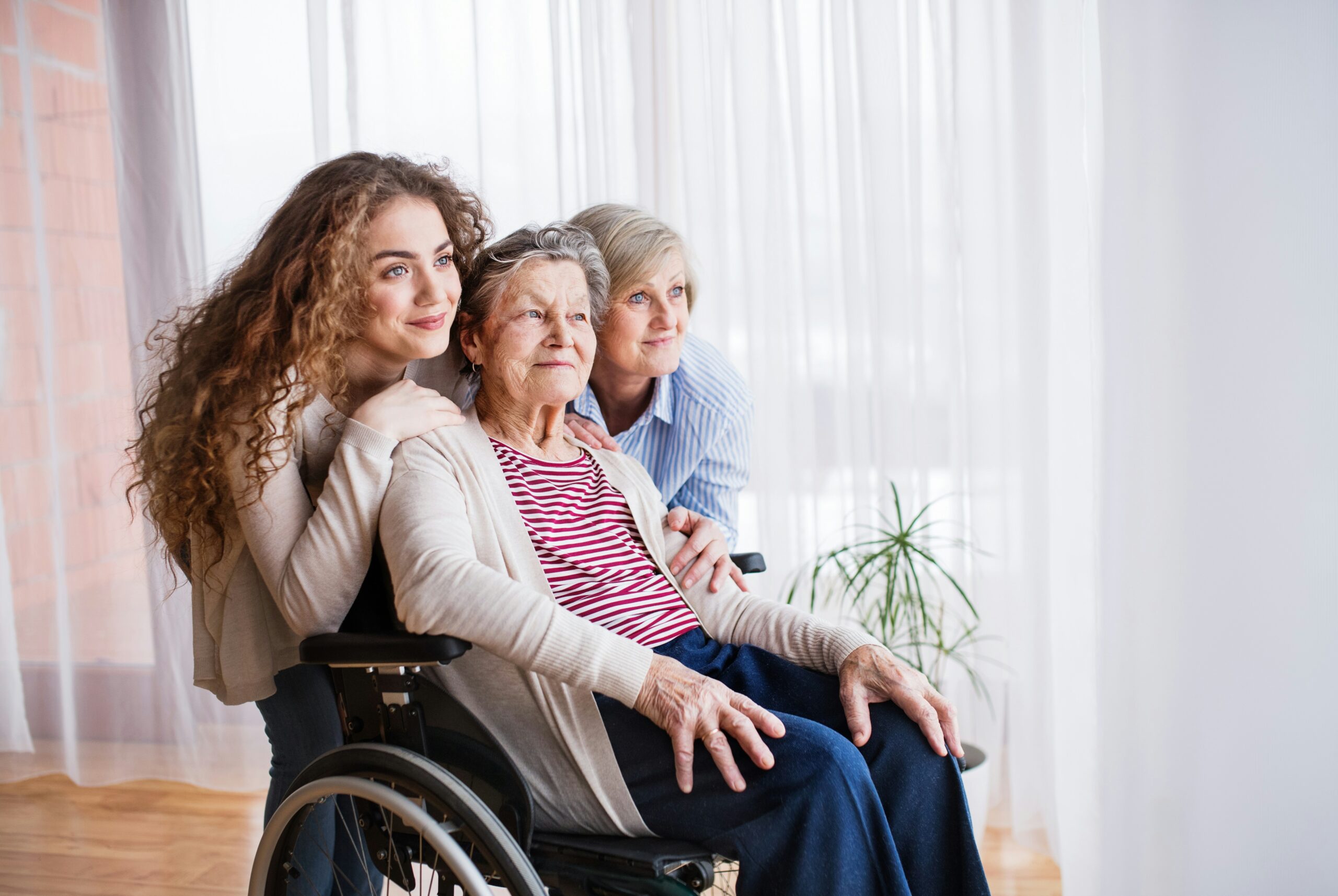 Two women stand beside a smiling elderly woman in a wheelchair.