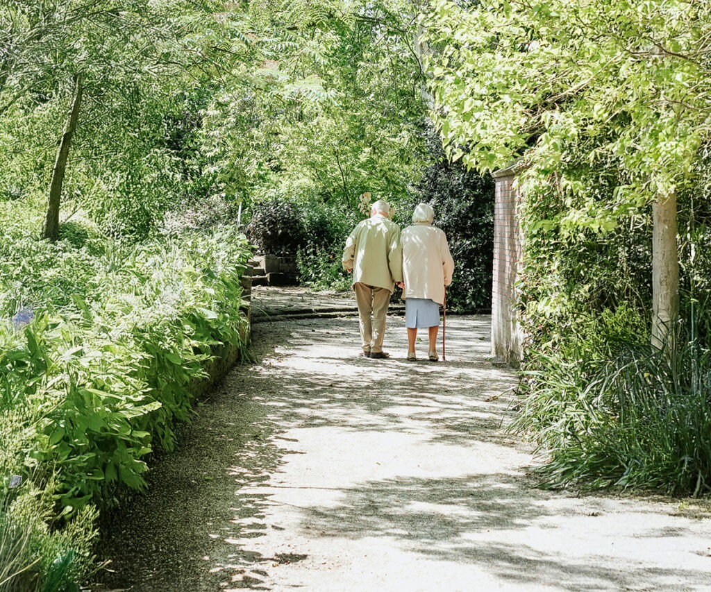 Elderly couple walks hand in hand on a scenic path.